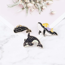 Detailed view of three enamel whale pins on white marble surface with dried flowers