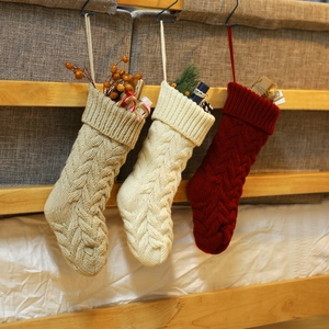 Three cable knit Christmas stockings in beige and red hanging with festive decorations