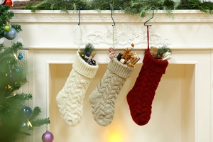 Close-up of cable knit Christmas stockings in ivory, oatmeal, and burgundy hanging by fireplace