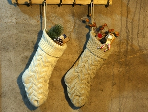 Detail of cable knit Christmas stockings with pinecones and ornaments on wood hooks