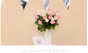 Pink and white faux roses in a white ceramic vase under gold party banner decor
