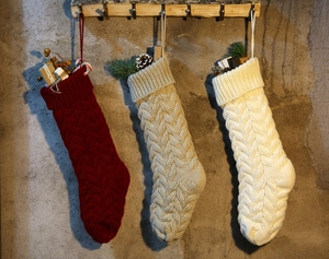 Close-up of cable knit Christmas stockings in red, beige, and white on a wooden rack