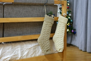 Close-up of cable knit Christmas stockings in beige and white hanging on wood