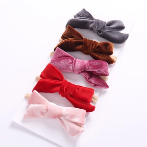 Close-up of five velvet bow headbands in grey, brown, pink, and red on white card