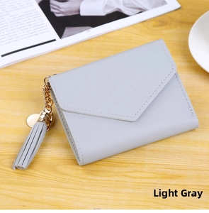 Detail of light grey short leather wallet with tassel pendant on a wooden table