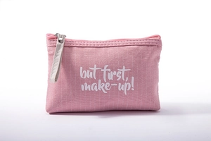 Pink canvas makeup bag with white 'but first, make-up!' lettering and silver metal zipper