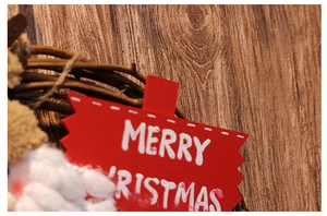 Detail of Christmas wreath featuring red Merry Christmas sign and Santa plush ornament