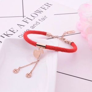 Detail of red braided rope bracelet with rose gold fortune bag and coin charms