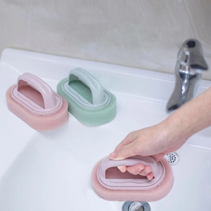 Close-up of pink and green long handle dish sponge brushes cleaning a white sink surface