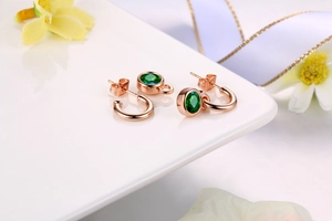 Detail of rose gold earrings featuring a round green gemstone and small hoop on a white stand