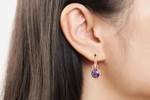 Close-up of a model wearing a rose gold hoop earring with a round purple zircon pendant
