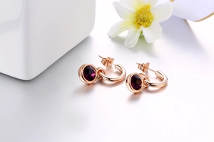 Detail of rose gold hoop earrings featuring deep purple round crystal drop pendants