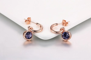 Detailed view of rose gold plated earrings featuring purple crystal pendants on white ceramic