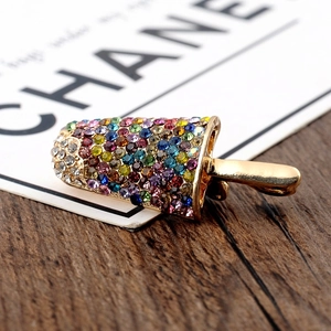 Macro shot of gold popsicle brooch with colorful rhinestones on a dark wood background