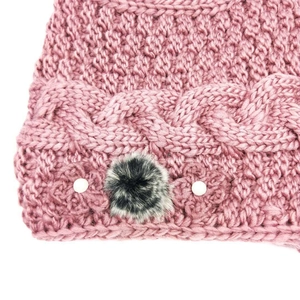 Detail of pink knit winter hat with thick cable pattern and faux fur flower decoration