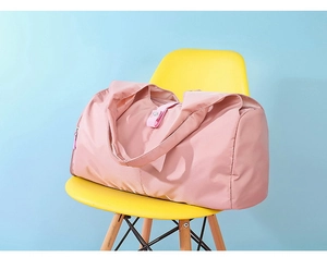 Detail of pink waterproof nylon travel bag showing durable handles on a yellow chair