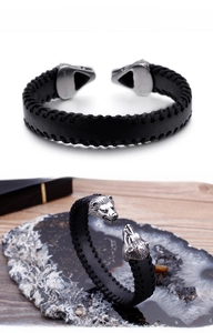 Detail view of woven black leather bracelet with silver wolf head ornaments on wooden surface