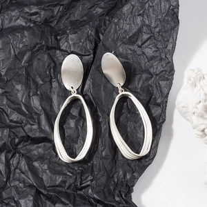 Close-up of geometric matte silver earrings with layered oval design on black background