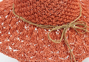 Detail of rust red handwoven straw hat showing hollow patterns and bow ribbon