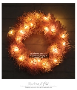 Nahaufnahme von rosa Lametta-Weihnachtskranz mit warmweißen LED-Lichtern auf dunklem Grund