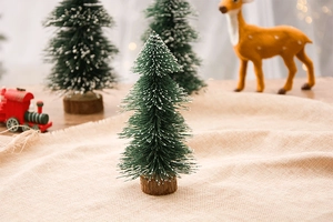 Miniature flocked green cedar Christmas tree with white snow and wooden base on burlap