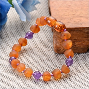 Detail of amber and amethyst baby bracelet on rustic wood with a blue floral accent