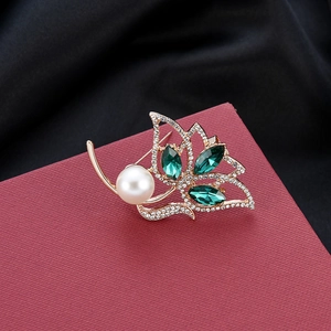 Detailed macro of gold-plated leaf brooch with white pearl and green marquise stones