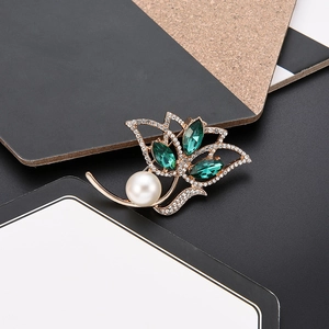 Macro shot of gold flower brooch with green gemstones, white zircons and a round pearl