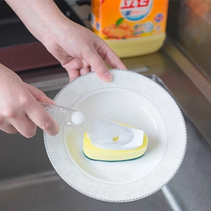 Action shot of long-handle dish brush with sponge head cleaning a white ceramic plate
