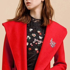 Elegant peacock brooch with blue and red crystals on red wool coat with black lace shirt