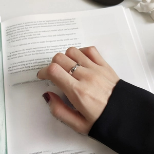 Close-up of a silver Mobius ring worn on a hand against a minimalist book background