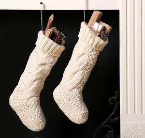 Detail of cream cable knit Christmas stockings filled with gift boxes and pinecones