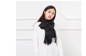 Close-up of black cashmere-like scarf with fringe tassels worn over a white knit sweater