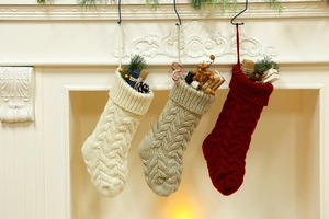 Detailed cable knit Christmas stockings in ivory, oat, and wine red hung on a mantel