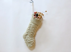 Close-up of beige cable-knit Christmas stocking with holiday gifts and candy canes