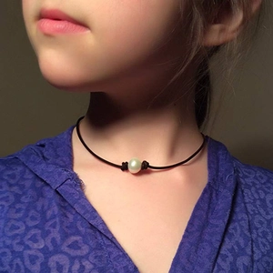 Close-up of a white freshwater pearl on a black leather cord necklace worn by a child