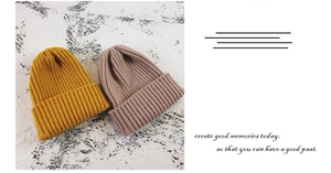 Detail view of ribbed knit beanies in ginger yellow and mauve with a folded cuff design