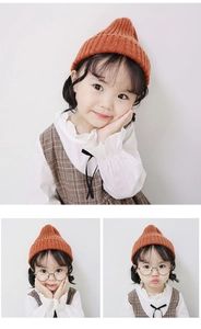 Detail of a bright orange knitted kids beanie paired with a checkered pinafore dress
