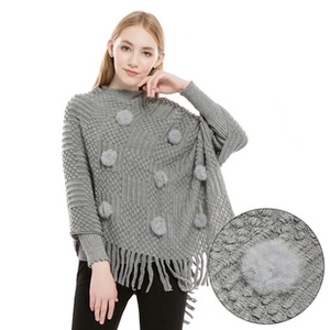 Detail of grey knitted chenille poncho with soft fur pompom and fringed hemline accents