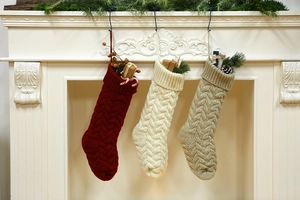 Three large knitted Christmas stockings in red, cream and khaki hanging on a white fireplace