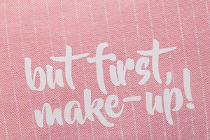 Detail of pink canvas makeup bag featuring 'but first, make-up!' white printed text