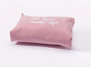 Detail of a pink striped canvas makeup bag featuring white but first make-up lettering