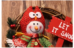 Close-up of snowman wreath with red knitted owl hat and 'LET IT SNOW' sign on wood background