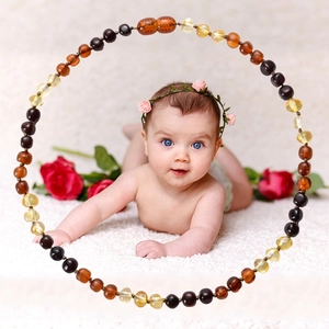 Natural amber baby necklace with colorful beads on a white faux fur rug with roses
