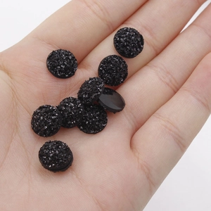 Detailed view of 10mm black sparkling resin druzy cabochons held in hand for size reference