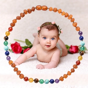 Colorful natural stone and amber baby necklace displayed on soft white faux fur background