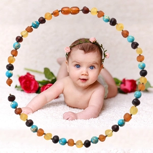 Natural amber and turquoise beaded necklace for babies on a soft white plush background