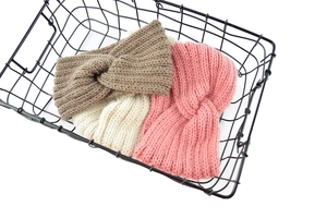Detail of twisted cable knit headbands in khaki, beige, and pink inside a wire basket