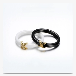 Detail of black and white ceramic rings with gold X-shaped diamond accents on metallic surface