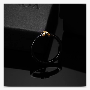 Close-up of black ceramic ring featuring a golden clover floral motif on a luxury box